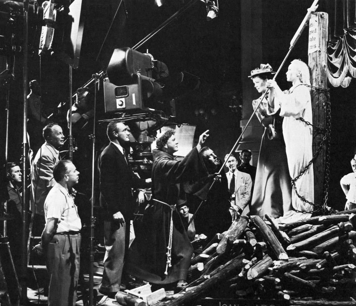 On the set are Sam Goode, boom operator; Marley; Norman McClav, best boy; Lothrop Worth, camera operator; DeToth; Red Turner, prop artist; star Vincent Price; Jimmy McMahon, assistant director; and star Phyllis Kirk with the effigy of St. Joan.