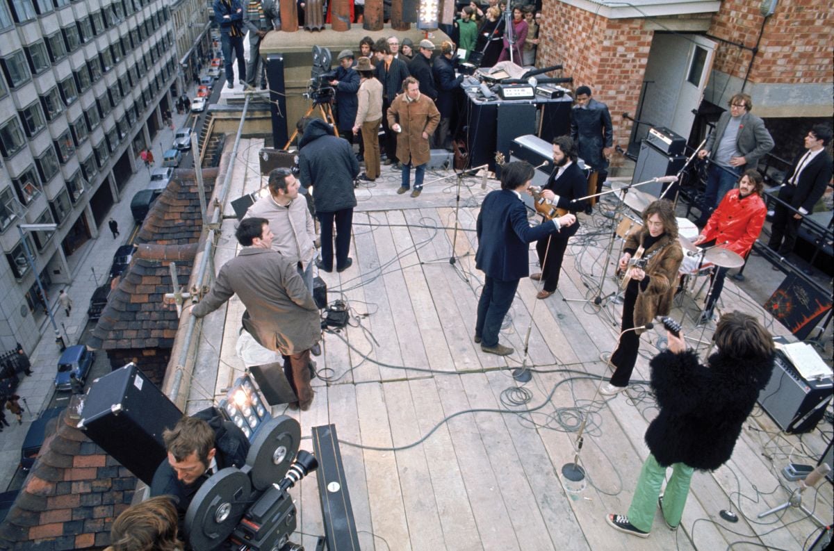 The Beatles prepare to perform their now-iconic rooftop concert in 1969 for the documentary Let It Be. Director Michael Lindsay-Hogg stands directly in front of the band, and Richmond is visible near the camera at top left, in brown hat and pants. (Photo courtesy of Disney and Apple Corps)