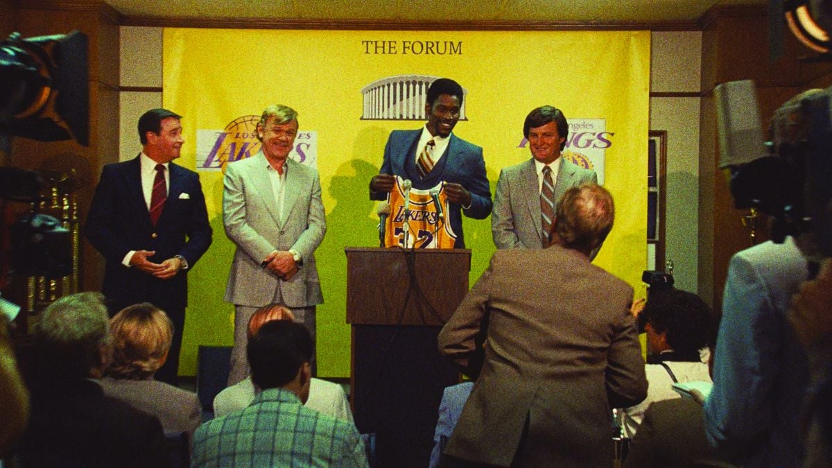 After being drafted by the Lakers, Magic is introduced to the press by the team’s broadcast announcer and assistant GM, Chick Hearn (Spencer Garrett, far left); incoming owner Jerry Buss (John C. Reilly); and coach Jerry West (Jason Clarke).