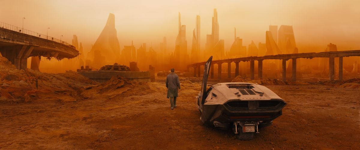 K (Ryan Gosling) steps away from his "spinner" car toward a bleak and brutal landscape.