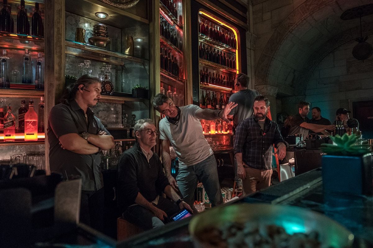 Director Chad Stahelski (wearing white shirt) and Laustsen confer behind the bar of the Continental Hotel — actually the interior of the former Williamsburgh Savings Bank tower in Brooklyn. “I needed someone who could light fast, because the more time I spend on lighting, the fewer takes I get,” says the director. “And not just someone who’s going to light for me — he’s got to be a world-creator. Dan was a big part of how we designed the film, even down to how we built our sets.”