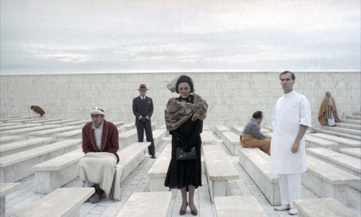 With his mother (Carla Mignone, center), Fascist state operative Marcello Clerici (Jean-Louis Trintignant; standing, in suit and hat) visits his father at an insane asylum. These scenes were filmed at the Piazza John Fitzgerald Kennedy, in the Palazzo dei Ricevimenti e dei Congressi dell’EUR, in Rome, Italy.