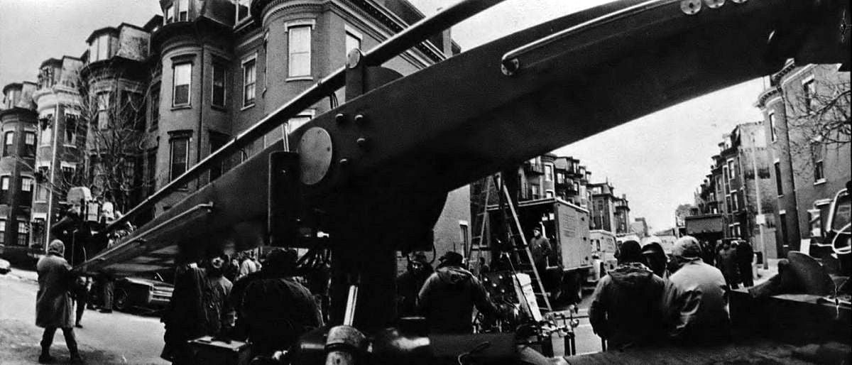 A Chapman camera crane, with Panavision camera mounted, dominates the scene as 20th Century-Fox crew films The Boston Strangler on location. Peculiar apparent distortion of the crane is due to the extreme wide-angle “fisheye” lens used to take the photograph.
